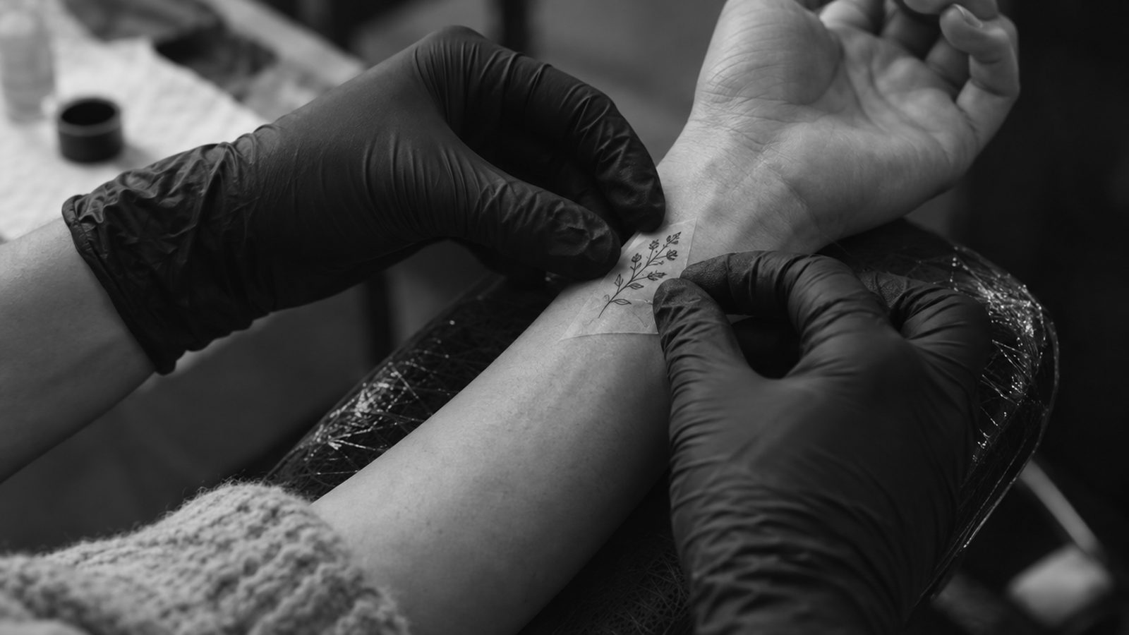 Illustration générée par IA : tatoueur ganté posant un pochoir sur le poignet d’une cliente