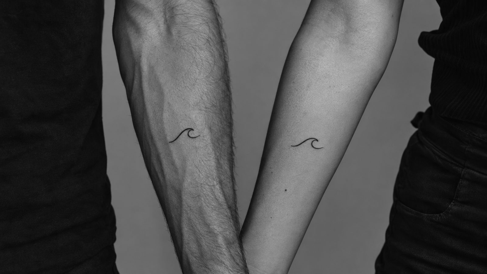 Illustration générée par IA : deux avant-bras avec le même petit tatouage de vague, noir et blanc