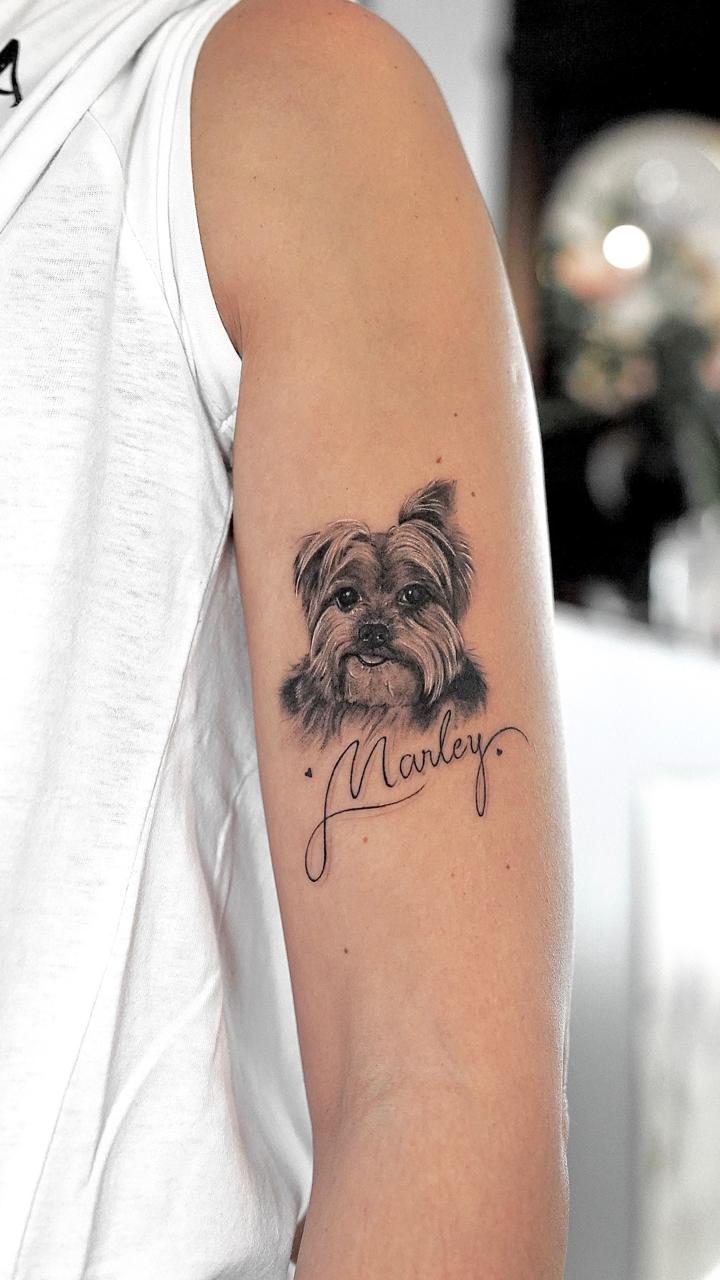 Portrait tatoué d’un chien avec le prénom Marley en lettrage cursif sur le bras, par Kako Tattoo
