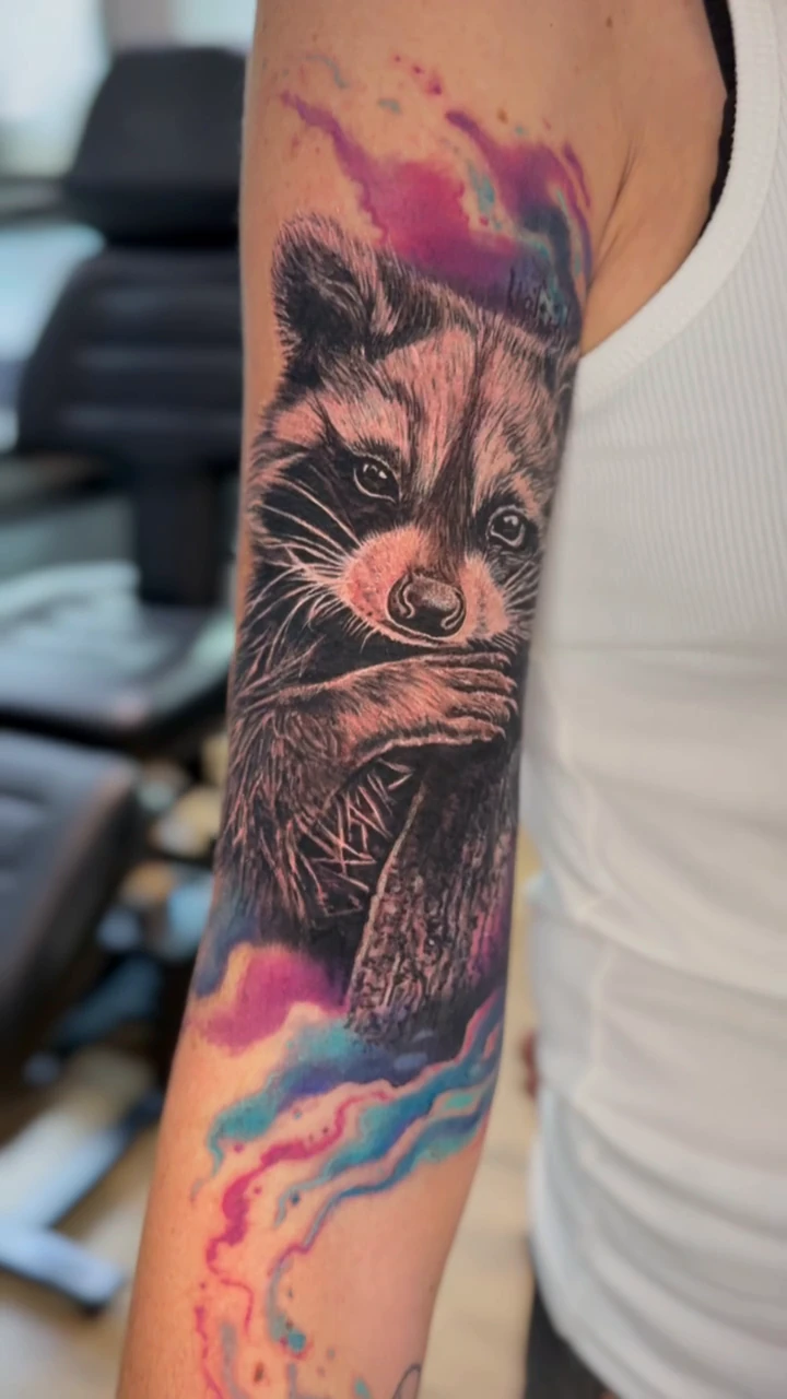 Raton laveur avec des touches de couleur sur le bras, par Kako Tattoo à Genève