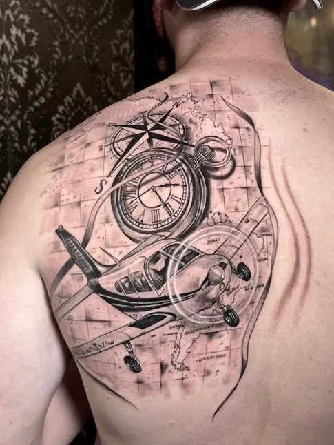 Avion, boussole et montre en noir et gris sur le dos, par Kako Tattoo à Genève